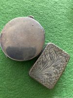 Closed view of two sterling silver trinket boxes showing etched surface details on green fabric background.