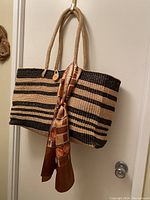 Front view of hand-woven tote bag with black and natural stripes, showing twisted rope handles and tied decorative scarf.