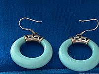 Front view showing both earrings with turquoise hoops and silver detailing on a blue background.
