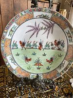 Full view of the large vintage Asian porcelain plate showing hand painted roosters and floral design with geometric border