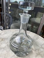 Front and angled view of the clear vintage glass decanter showing its stopper and rounded shape.