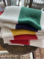 Folded knit couch throw showing stacked multicolor stripes in green, navy, yellow and red on a white knit background.