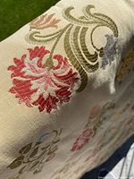 Close-up of embroidered floral patterns in red, green, and purple on beige textured tapestry fabric.