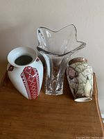 Front view of three vases: one white ceramic with red pattern, one clear glass with wavy top, one crackle glazed ceramic.
