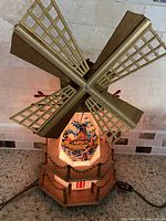 Front view showing rotating wooden lattice sails and illuminated base with painted Dutch maritime scene.