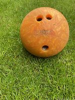 Orange Brunswick bowling ball with finger holes on grass, showing embossed branding.