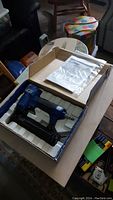 Blue and black Campbell Hausfeld brad nailer in box with manual on top.