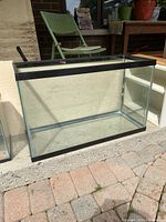 Clear rectangular glass aquarium placed outdoors on a brick surface with metal frame around edges.