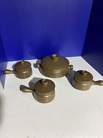 Full set of one large casserole dish with lid and three smaller handled bowls with lids, all brown ceramic.
