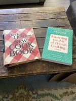 Both cookbooks together on a wooden table, showing Better Homes and Gardens New Cookbook and Mastering the Art of French Cooking by Julia Child.