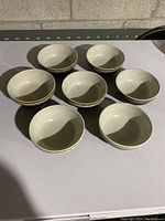 Seven brown and cream Denby Artisan bowls arranged in a group on a flat surface, showing top view to display the interior cream glaze.