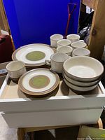 Display of mugs, bowls, and plates with various earthy colors in a white tray.