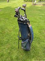 Full view of blue golf bag standing on grass with various golf clubs inside