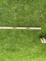 Full length image of the wooden level lying on grass, showing its metal framing and three bubble vials.