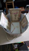 Open hat box showing spiral notebooks with floral designs, cards, and envelopes inside
