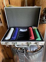 Open stainless steel case showing five stacks of poker chips in white, blue, red, green, and black, with two sets of white dice with black dots in center compartment.