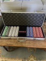 Open metal case showing five stacks of wrapped poker chips in green, black, white, blue, and red colors with two red dice in the middle