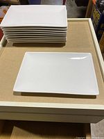 Stack and single view of 10 white rectangular plates with smooth surfaces and rounded edges.