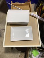 Stack of ten white rectangular plates with one plate placed adjacent to show shape and design.