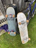 Two full skateboards leaning against a bike and wooden fence, showing general wear and orange wheels.