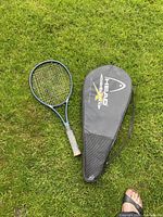 Full photo showing Prince tennis racket and Head case lying on grass, image includes angle showing grip and strings of racket and case surface details.