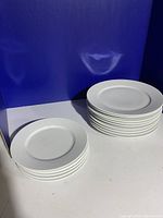 Two stacks of white ceramic plates shown from above and side. One stack smaller plates, one stack larger plates.