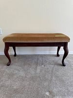 Antique wooden bench with curved legs and brown upholstered seat shown from the front.