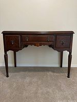 Front view of antique wooden desk showing three drawers with ornate handles and keyholes, tapered legs, and scalloped apron.