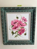 Photo of a framed floral painting depicting pink flowers with green buds and leaves in a teal decorative frame.