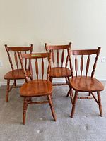 Set of four wooden dining chairs arranged in a group showing their spindle backs and turned legs.