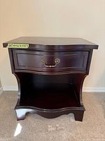 Front view of the dark wood nightstand showing single drawer with ornate handles and open shelf below