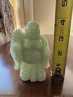 Photo shows a small light green jade Buddha statue standing next to a measuring tape indicating a height of about 4 inches.