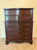Full front view of tall boy dresser showing five drawers with brass-tone handles and dark wood finish.