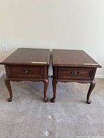 Two brown wooden side tables with rectangular tops, single drawers, and curved legs.