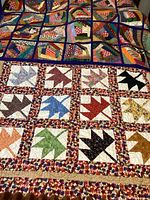 Image showing two quilts laid out, one with colorful geometric blocks and the other with maple leaf blocks bordered with floral print fabric.