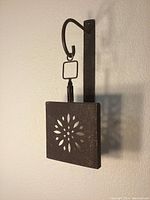 Side view of one sconce showing the curved mounting arm and floral cut-out metal panel.