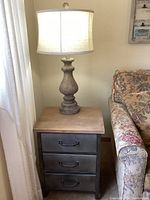 End table with wooden top and three metal drawers, showing side next to couch.