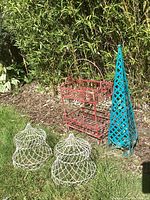 Photo showing all four items together outside: two white wire cages, red two-tier metal cart, blue lattice tower, outdoors in daylight against greenery.