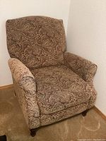 Front view of warm-toned paisley recliner chair showing full upholstery and wooden legs.