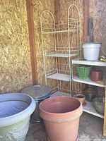 Overall lot showing large ceramic and terracotta pots with tall white wire shelving unit and shorter white metal shelf.