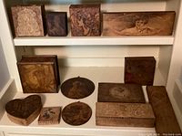 Wide shot showing all wooden boxes arranged on two shelves, highlighting various sizes and detailed female portraits burnt into wood.