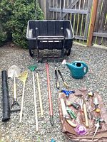 Photo showing full set of gardening tools and two-wheeled plastic garden cart on gravel surface.