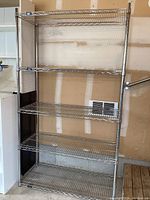 Full frontal photo showing entire steel frame storage shelf with five wire shelves against a wall with garage interior visible.