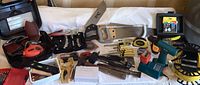 Overall view of assorted tools including Black & Decker electric sander, hand saw, cordless drill, measuring tape, screwdrivers, clamps and drill bit sets arranged on white cloth.