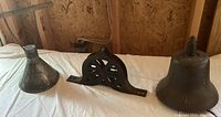 Three items side by side on table: metal cone funnel, decorative pulley block, ship bell