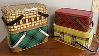 Four vintage metal picnic baskets grouped together showing different patterns and handle styles.