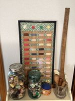 Full view of lot including framed vintage sewing notions, jars with buttons and thread spools, pin cushion, wooden sewing tools, and ruler.