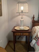 Full view of vintage wooden side table with burl veneer drawer, white metal lamp with sheer mesh shade, and decorative painted metal tray on top.