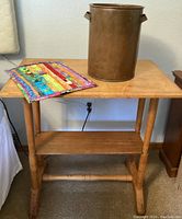 Wide shot of the wooden two-tier side table with copper can and quilted textile decoration on top.