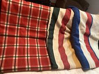 Red plaid blanket alongside cream blanket with red and blue stripes